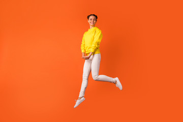 Fototapeta na wymiar Full size photo of pretty teenager moving jumping looking have smile on her face isolated over orange background