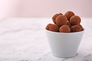 Tasty sweet truffles in bowl on light table