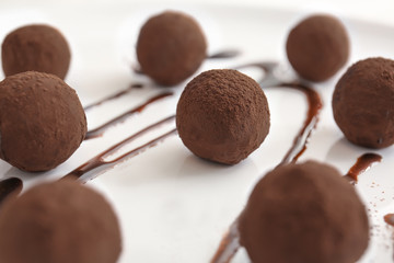 Tasty sweet truffles with chocolate sauce on plate, closeup