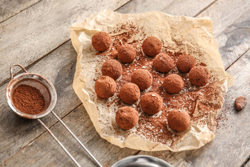 Parchment with tasty sweet truffles and cacao powder on wooden table