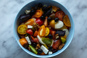 Salad of different types of tomatoes with mozzarella, feta, and olives. Ready with basil and nuts.