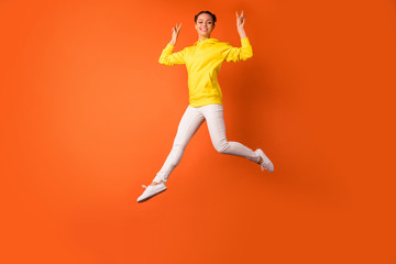 Fototapeta na wymiar Full body photo of cheerful lady making v-signs smiling jumping isolated over orange background