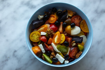 Salad of different types of tomatoes with mozzarella, feta, and olives. Ready with basil and nuts.