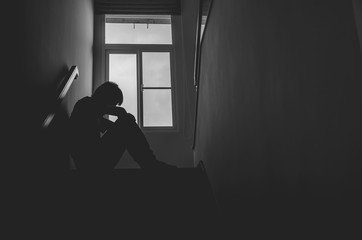 Silhouette Sad young man sitting at the stairs in the dark, Depression and anxiety disorder concept, Life problems, illness,Sadness, despair, dark..