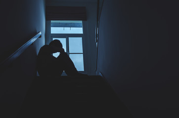 Silhouette Sad young man sitting at the stairs in the dark, Depression and anxiety disorder concept, Life problems, illness,Sadness, despair, dark..