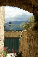 View of the Mont Ventoux through a porch of the village of Faucon. Ventoux mountain. In the foreground a street light, a door, flowers, a tree, a facade. Spring in France, Provence, Vaucluse.
