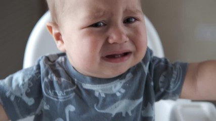 One year old baby boy cries, close-up. Babyboy crying in highchair.