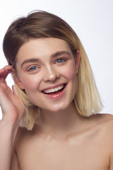 Naklejka premium Closeup of beautiful young woman's face with clean perfect skin and hair smiling at camera. Portrait of a blonde with blue eyes. Spa, skin care and wellness. Isolated on white background