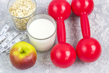 A glass of milk and a glass of oat flakes (rolled oats). Apple with measuring tape and dumbbells