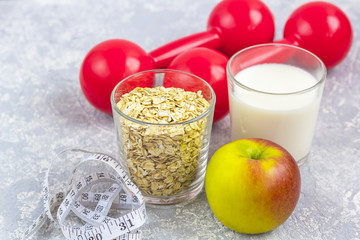 A glass of milk and a glass of oat flakes (rolled oats). Apple with measuring tape and dumbbells