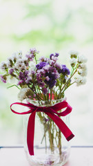 A bouquet of dried violet, pink and white wildflowers are in a transparent vase with a bright red bow. Bright flowers lit by sunlight. Soft selective focus, macro flowers. Photo background.