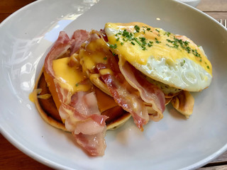 Salty Pancakes with Hollandaise Sauce, Melted Cheddar Cheese, Eggs and Crispy Bacon for Breakfast. Salted Food.