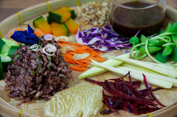 Yummy Thai southern rice salad with mix vegetables and spicy sauce in bamboo container on wooden background.