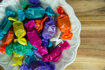 Top view beautiful colorful wrapped candies on white dish.