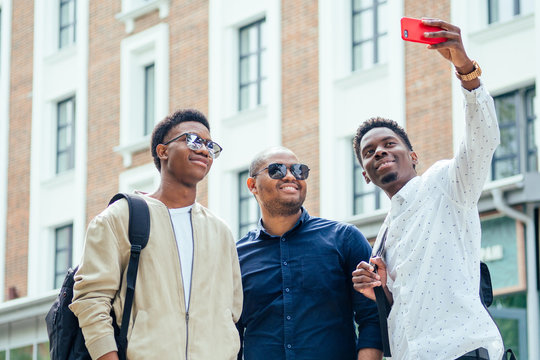 a group of three fashionable cool African American guys students communicating on the street looking at smartphone take pictures selfie on phone in street