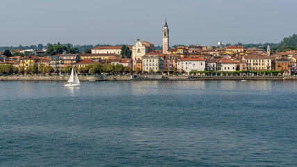 Obraz premium Beautiful view of Arona, Novara, Italy, with a sailboat sailing on Lake Maggiore
