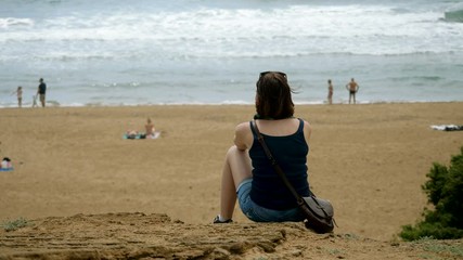 Beautiful young woman sitting on a sandy beach and looking at the Mediterranean sea. 4K