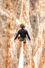 Fototapeta premium A man is walking along a stretched sling. Highline in the mountains. Man catches balance. Performance of a tightrope walker in nature. Highliner on the background of valley.