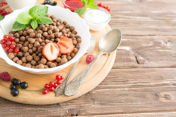 Bowl of healthy corn flakes breakfast cereal topped with fresh blackcurrants and strawberries served in a white ceramic bowl for a delicious meal Healthy tasty breakfast chocolate balls.
