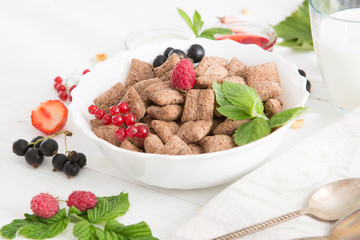 Bowl of healthy corn flakes breakfast cereal topped with fresh blackcurrants and strawberries served in a white ceramic bowl for a delicious meal Healthy tasty breakfast chocolate square pads