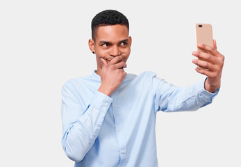 African Amerfican young man holds modern smart phone, speaking online and blogging on cellphone. Handsome male smiling and reading news in Internet. People and technology concept