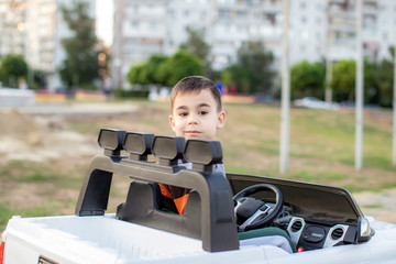 child boy is riding a white toys electric car in the park