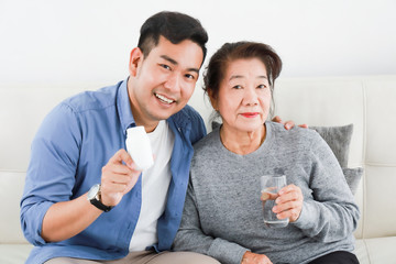 Asian senior woman mother with young man son with medicine and grass of water in living room