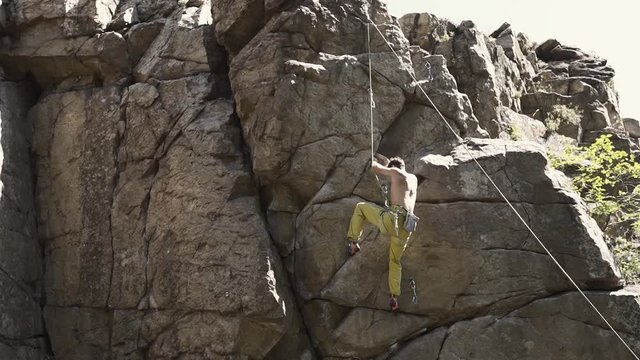 athletic arab or hindu man rock climber with naked torso climbs on a cliff with top belaying, searching, reaching and gripping hold. outdoor rock climbing and active lifestyle concept, FullHD stock