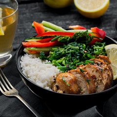 Buddha bowl meal with teriyaki chicken fillet, fresh vegetable salad, stew cabbage and basmati rice on a rustic table. Delicious dish in a black bowl with homemade lemonade.