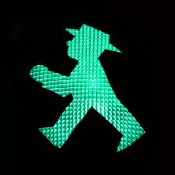 Green pedestrian traffic light with the iconic Ampelmann symbol of East Germany, Berlin isolated on black background