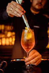 Elegant bartender is preparing pink cocktail holding orange chips at bar counter background.