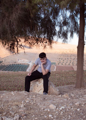 Teenager sits on a stone on nature background.