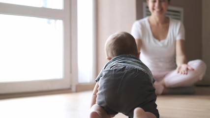 Little baby boy crawling on the floor at home near his mother. Cute happy ten month kid playing. Slow motion