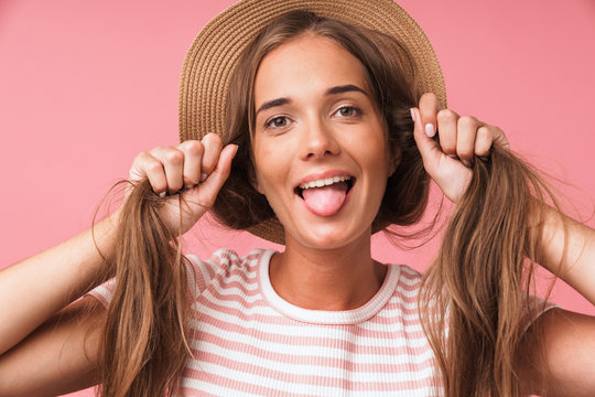 Image closeup of young cute woman wearing straw hat making fun with her hair and sticking out her tongue