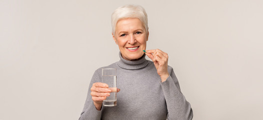 Beautiful elderly woman taking vitamin supplements over light studio background - obrazy, fototapety, plakaty