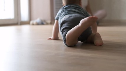 Baby boy crawling on floor at home in slow motion. Close-up of the baby's legs creeps to mother