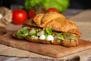 Croissant sandwiches served on wooden board. Croissants with egg, melted cheese, parsley, chicken ham, smoked salmon