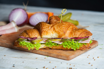 Croissant sandwiches served on wooden board. Croissants with egg, melted cheese, parsley, chicken ham, smoked salmon