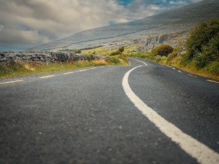 Small twisted road in Burren National park, Ireland, county Clare. Selective focus, low angle, Cloudy sky, Mountains in the background.