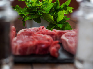 Fresh green mint in focus, lamb chops out of focus, image framed by salt and pepper shakers out of focus,