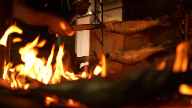 Medium pull-focus shot of placing a skewer of Saibling char fish next to a burning wood fire pit