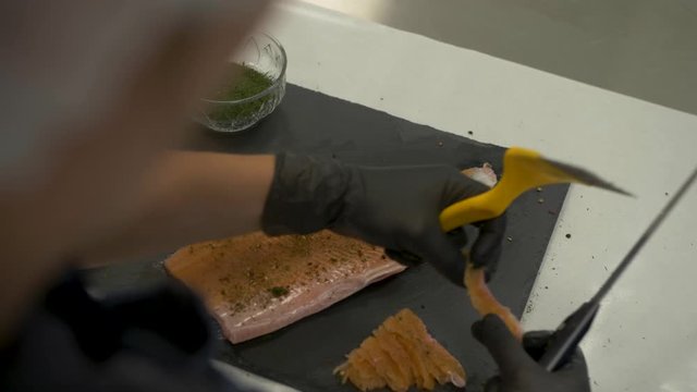 Handheld over the shoulder shot of an old fisherman filleting a Saibling Char shish with a sharp knife on a counter with small bowls of herbs and spices