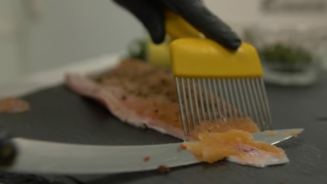 Extreme close-up shot of an chef filleting a Saibling Char shish with a sharp knife on a counter with small bowls of herbs and spices