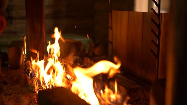 Medium close-up shot of placing a skewer of Saibling char fish next to a burning wood fire pit