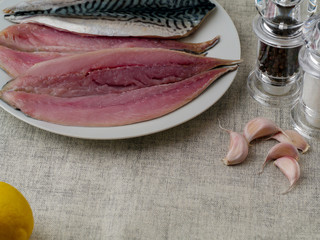 Still life, Fresh mackerel fillets on a white plate, Garlic cloves, lemon, salt and pepper shaker. Sea food preparation.
