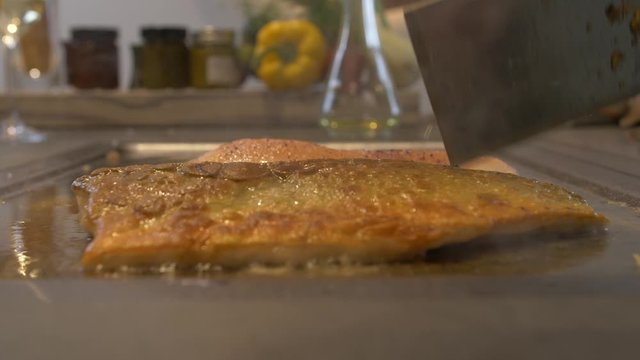 Extreme close-up handheld shot of Saibling Char fish fillets sizzling and then flipped on a griddle covered in seasoning