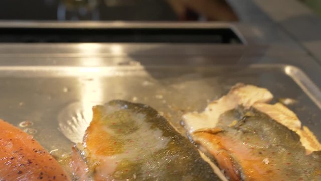 Handheld close-up shot Saibling Char fish sizzling on a griddle with a hand flipping and adding butter on to it