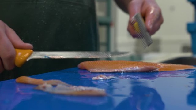 Handheld extreme close-up shot of a chef slicing and filleting pieces of a Saibling Char fish covered in seasoning on a kitchen counter