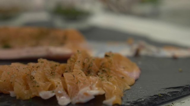 Handheld extreme close-up shot of a chef slicing and filleting pieces of a Saibling Char fish covered in seasoning on a kitchen counter