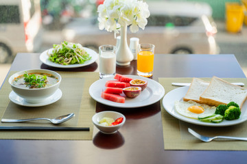 Fresh romantic breakfast table next to window with bread, fruit, juice, milk, noodle soup